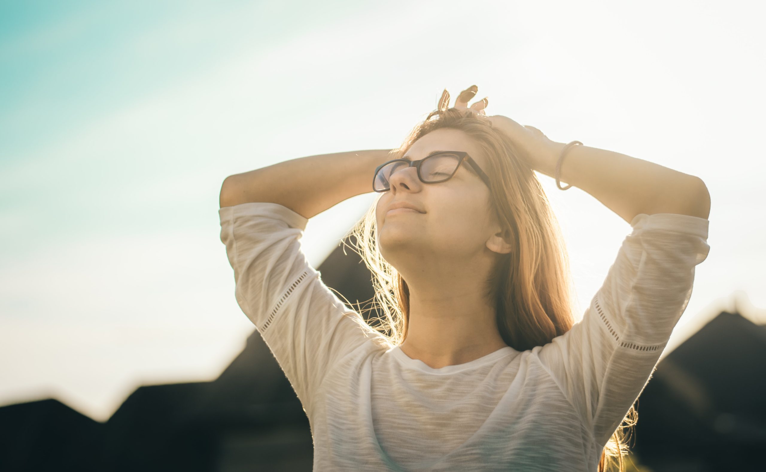 夕日を浴びながら屋外で目を閉じて深呼吸する、眼鏡をかけた女性
