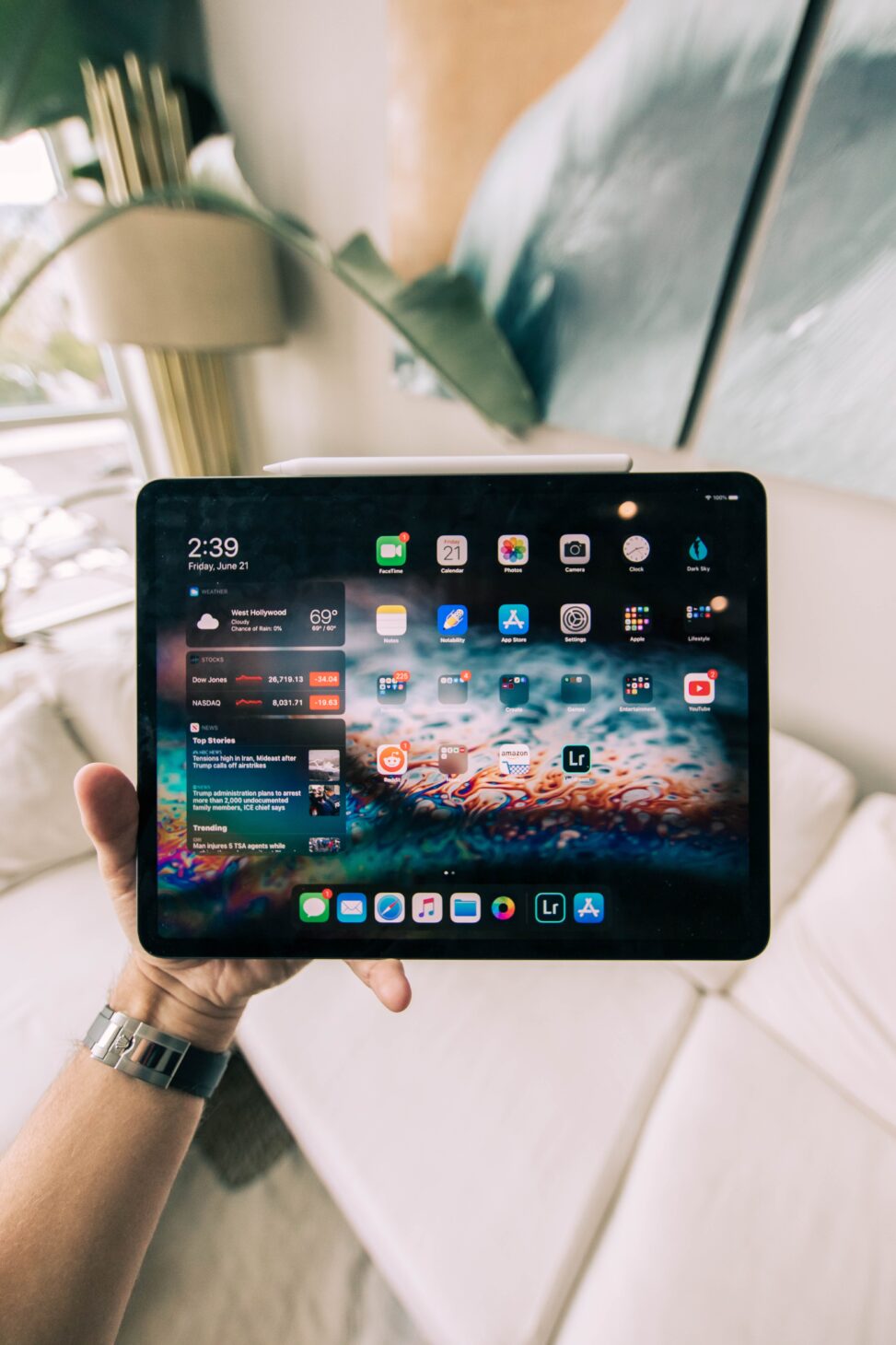 ソファでホームボタンのないiPadを両手で持ち、ホーム画面を表示している様子
