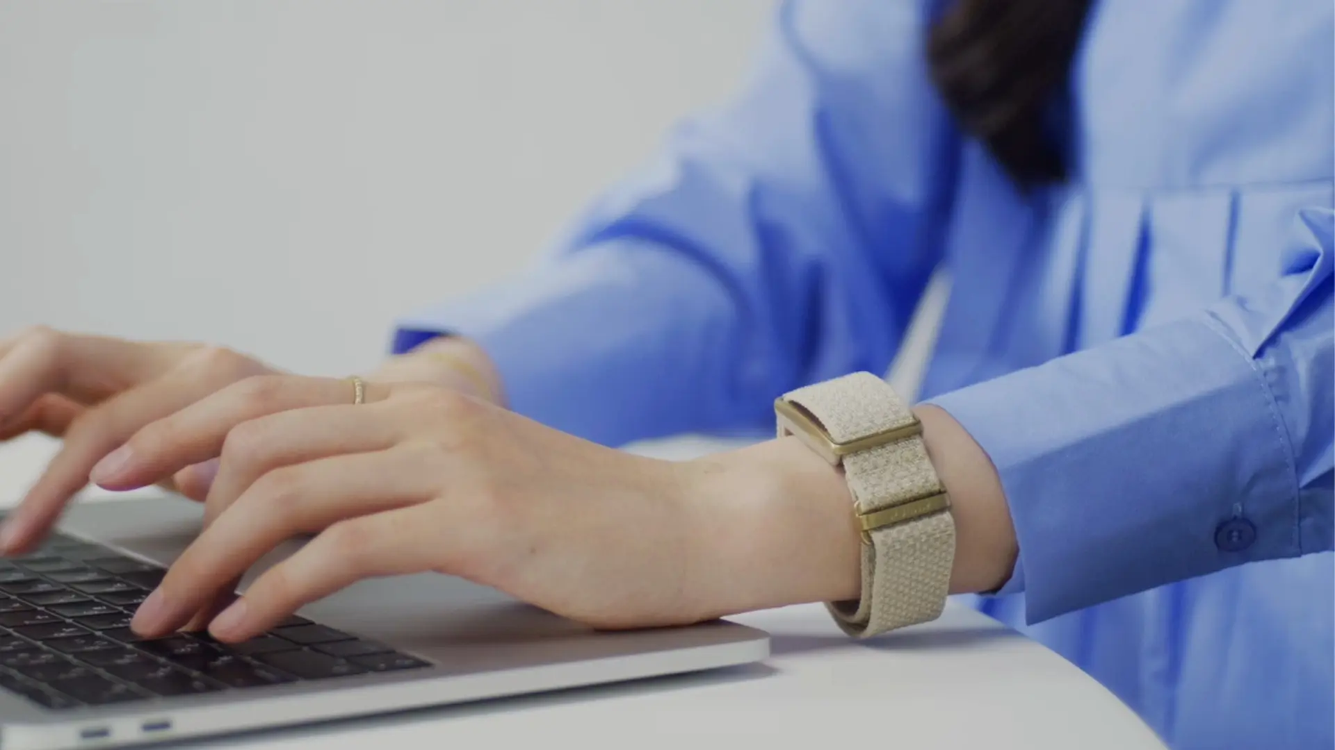 ノートPCで作業する女性の手首にベージュのスクリーンレス健康バンドPOLAR Loop