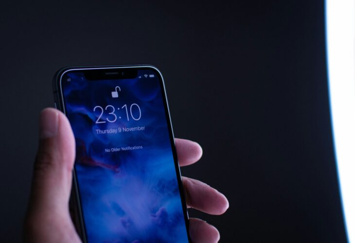 暗がりで時刻を表示したiPhoneのロック画面を手に持っている