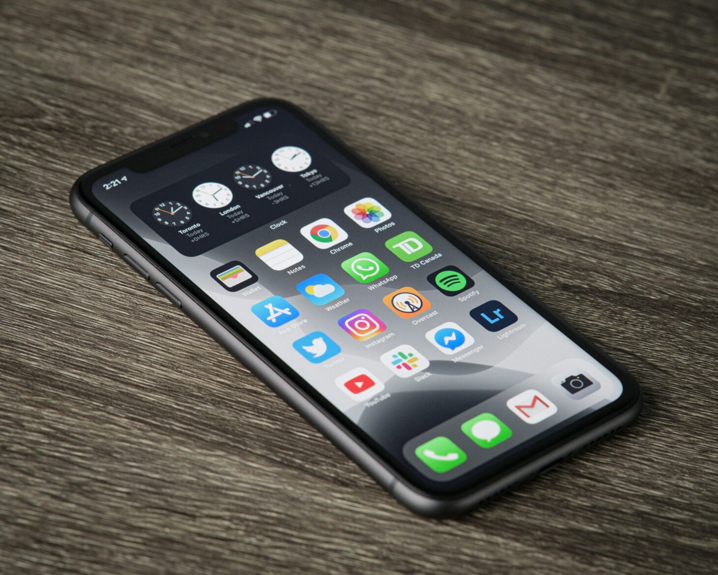 木の机に斜めに置いたノッチ付きiPhoneのホーム画面