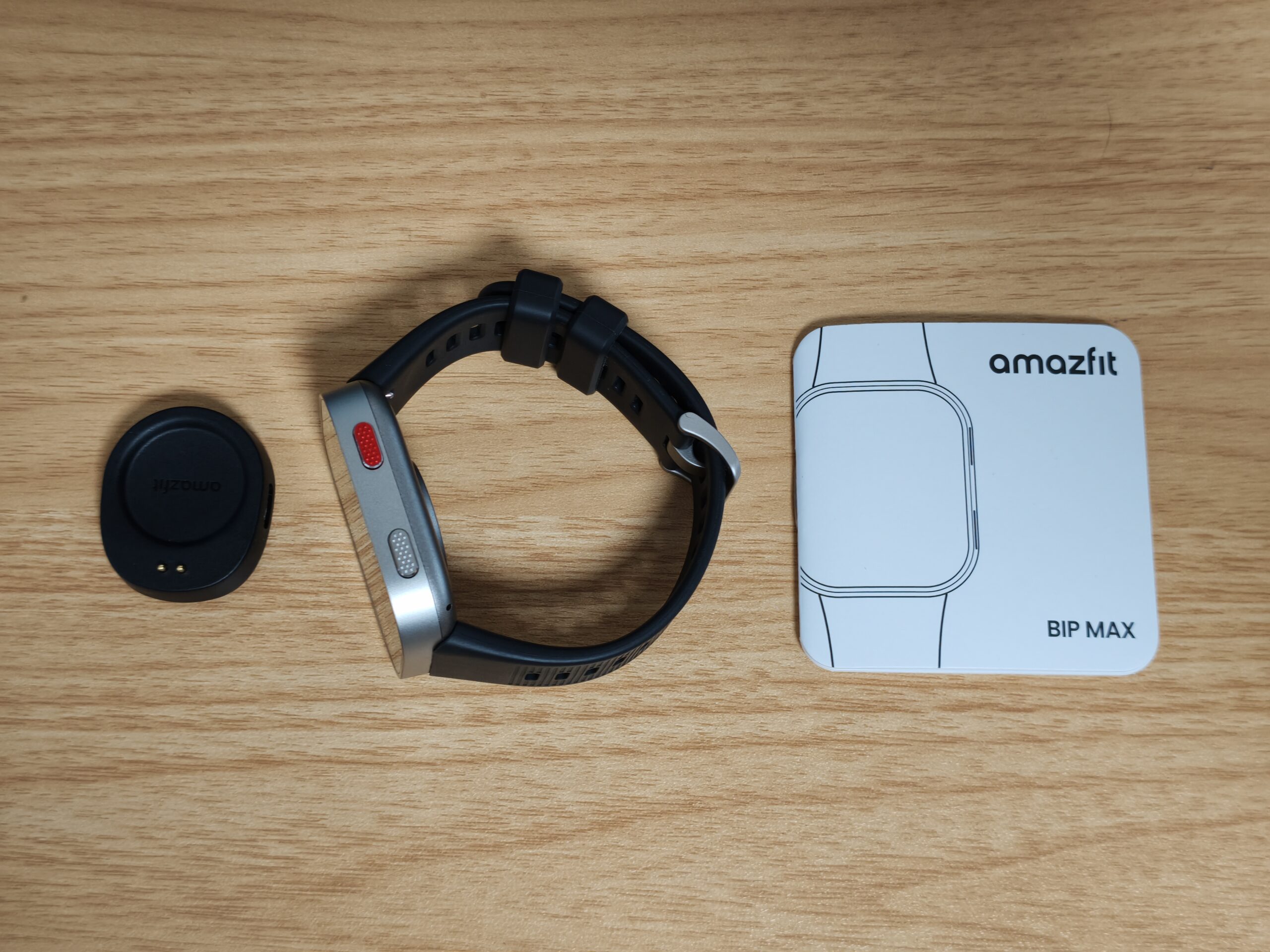 Amazfit Bip Maxの同梱物。マグネット式充電ベース、本体(バンド装着済)、取扱説明書「BIP MAX」を並べた写真