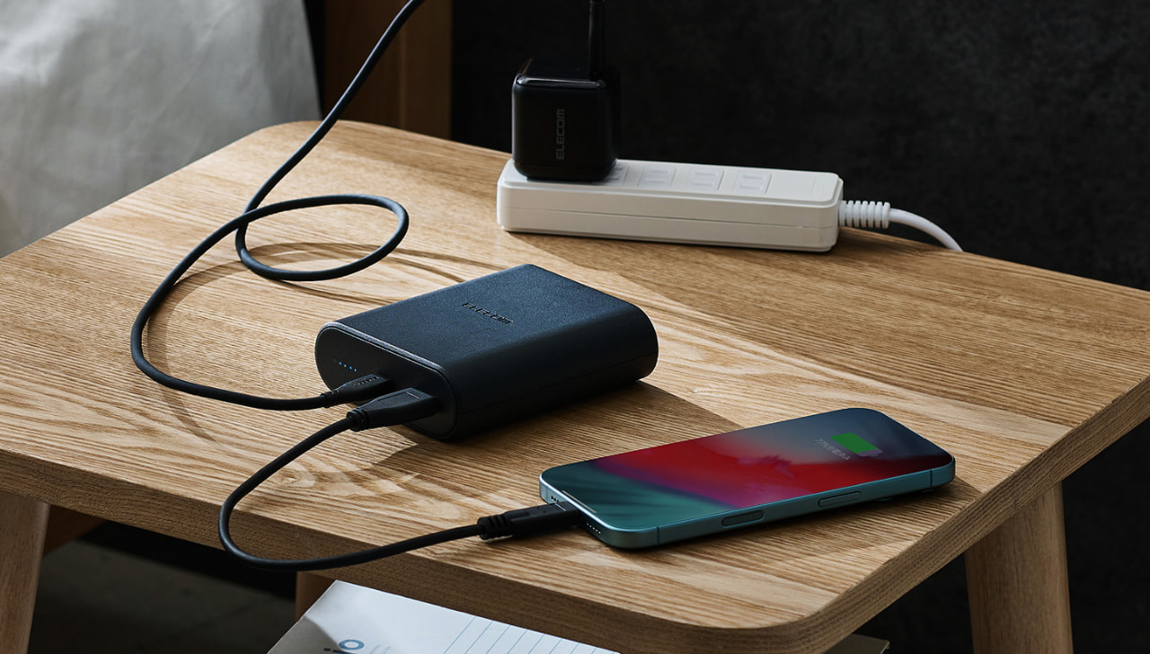 木の机に置かれたエレコム製モバイルバッテリーとiPhoneがケーブルで繋がり充電している卓上シーン