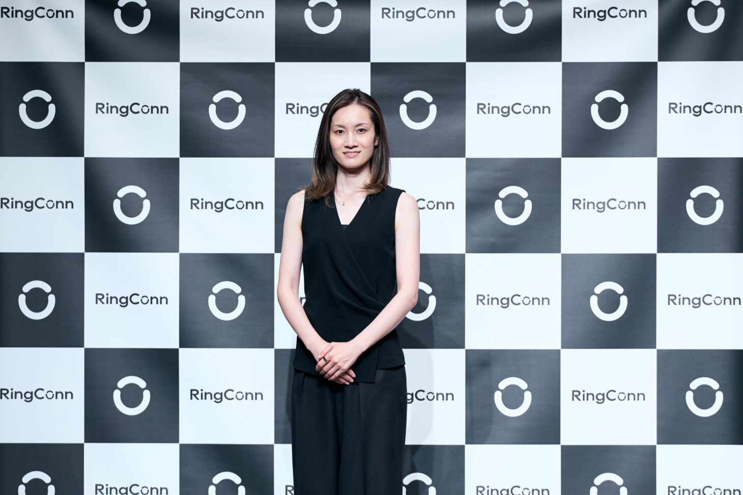 荒川静香さん 立ち姿オフィシャルポートレート。黒のノースリーブとパンツでRingConnロゴパネル前