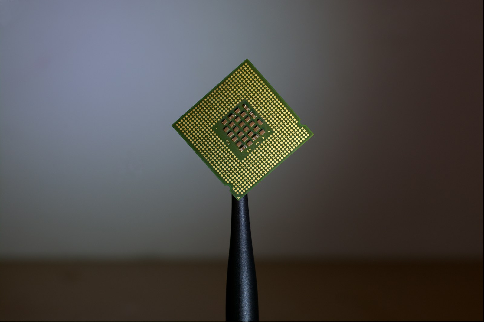 指でプロセッサ（CPUチップ）をつまんで持つクローズアップ写真。AppleとIntelのチップ製造提携噂のイメージ