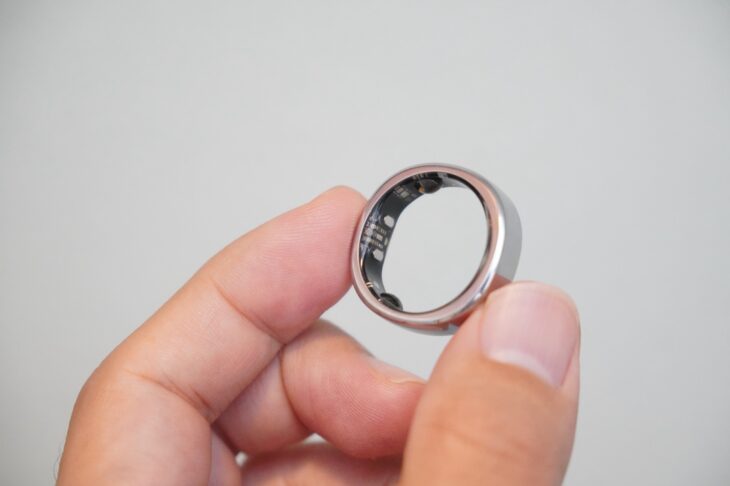 RingConn Gen 3 を指でつまんで持ち上げ、内側のセンサー面を見せたところ。内側は丸く、外側は四角い独自構造になっている
