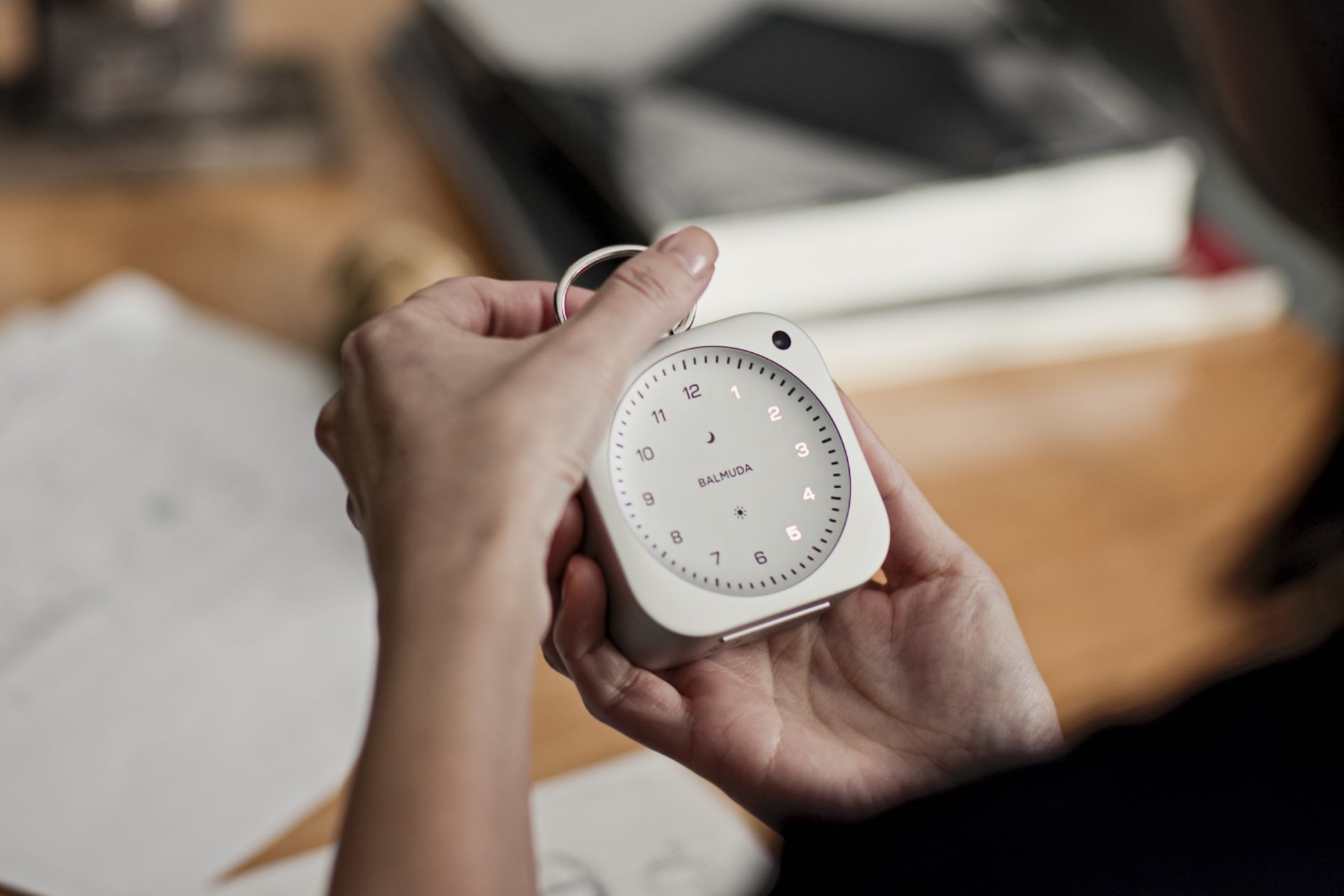 アルミニウム製のバルミューダ The Clock本体を手に持ったところ。針もガラスもない光の文字盤が見える