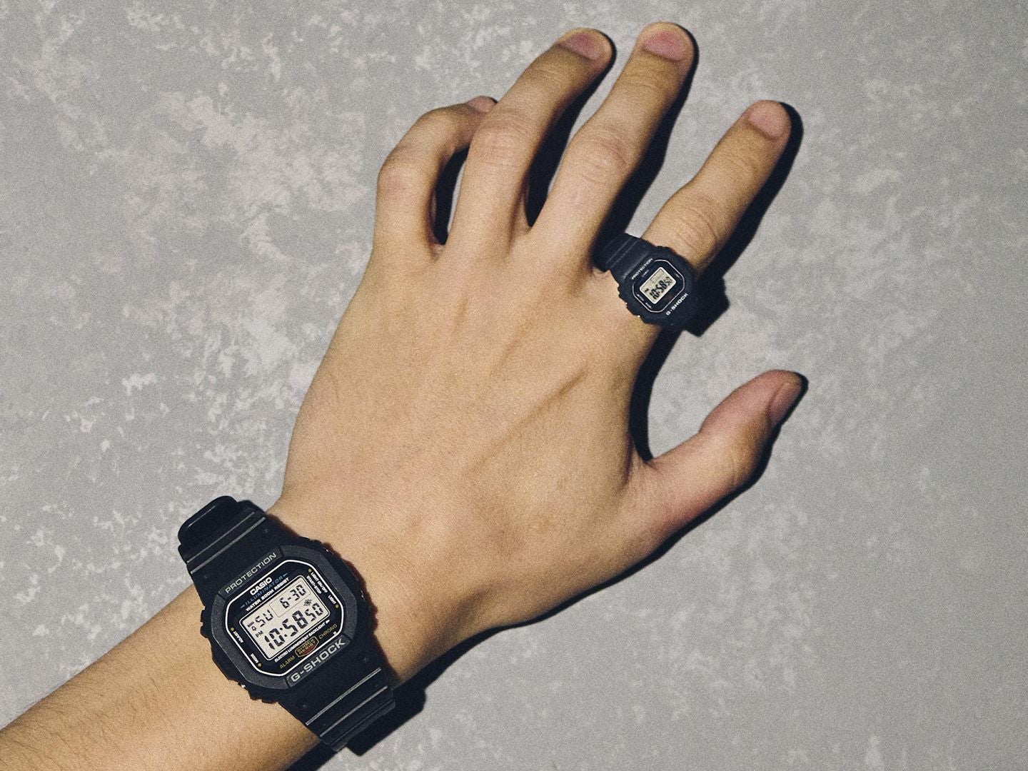 指に着けたDWN-5600と手首に着けた通常サイズのG-SHOCK DW-5600を並べて比較した写真