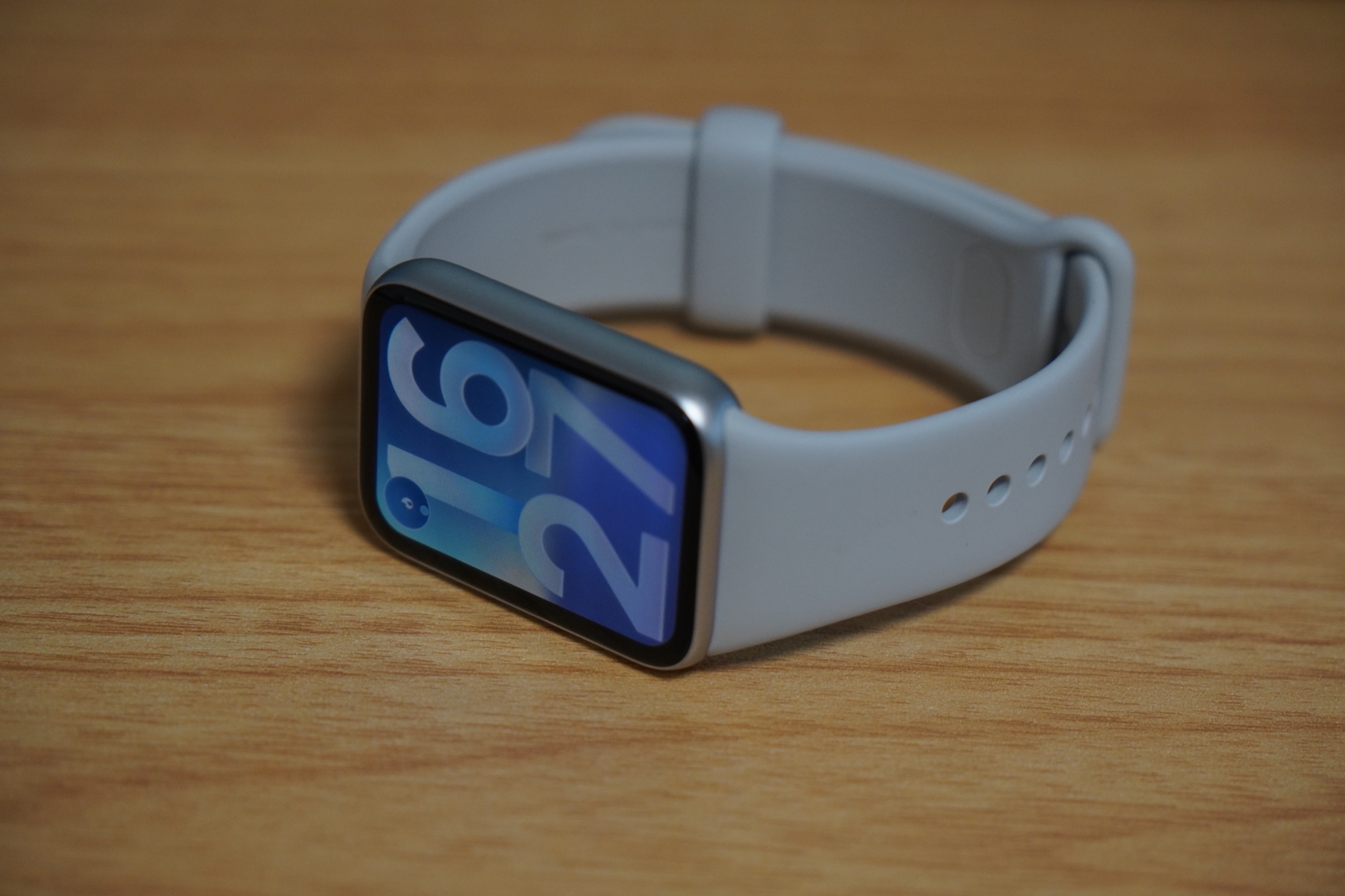机に置いた Xiaomi Smart Band 10 Pro シルバー。ブルーのウォッチフェイスと薄型ボディ