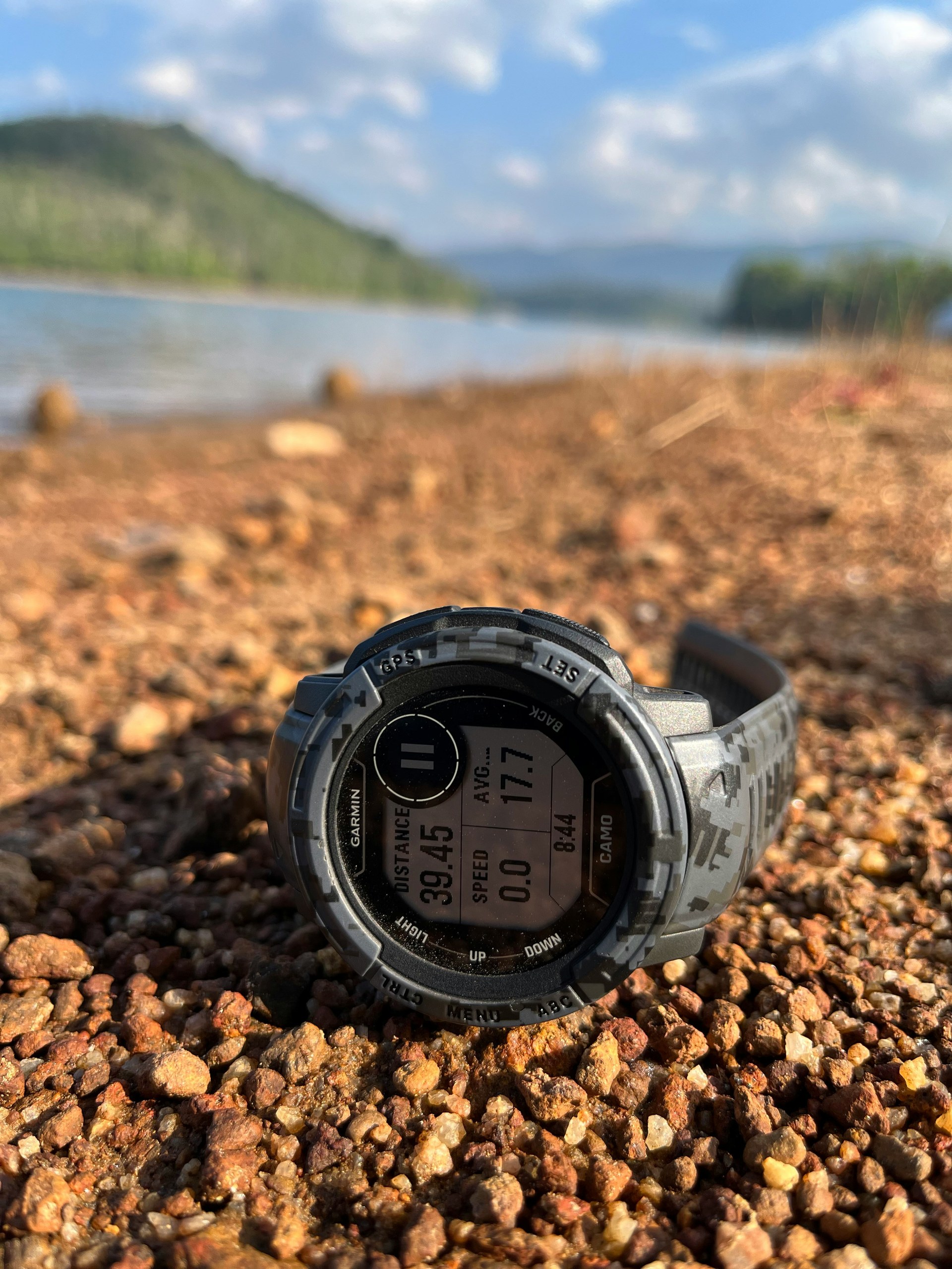 湖畔の砂利に置かれたGarmin Instinctスマートウォッチ