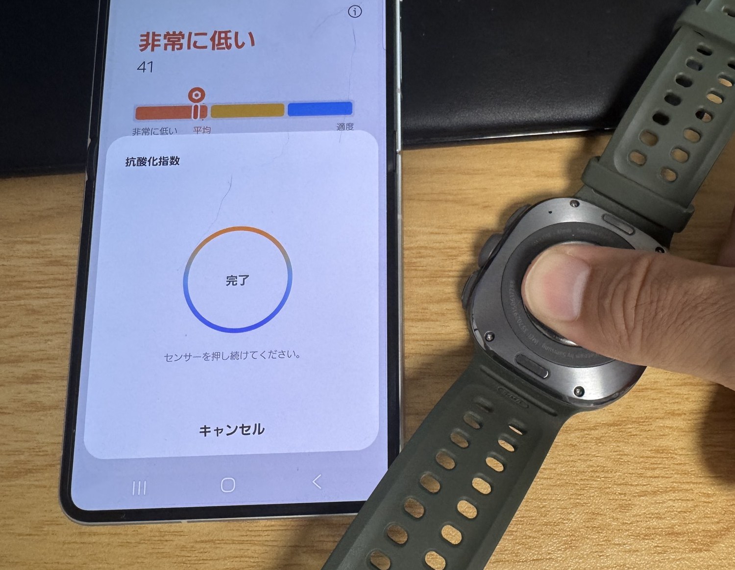 抗酸化指数の測定が完了した画面。スマートフォンに「完了」と表示され、結果は41で「非常に低い」。右手の親指はまだ時計の背面センサーに当てられている。
