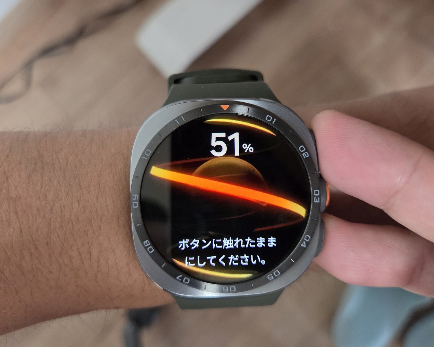 Galaxy Watch Ultra2で体組成を測定しているところ。時計のボタンに指を当てたまま、画面には進捗51%と「ボタンに触れたままにしてください。」と表示されている。