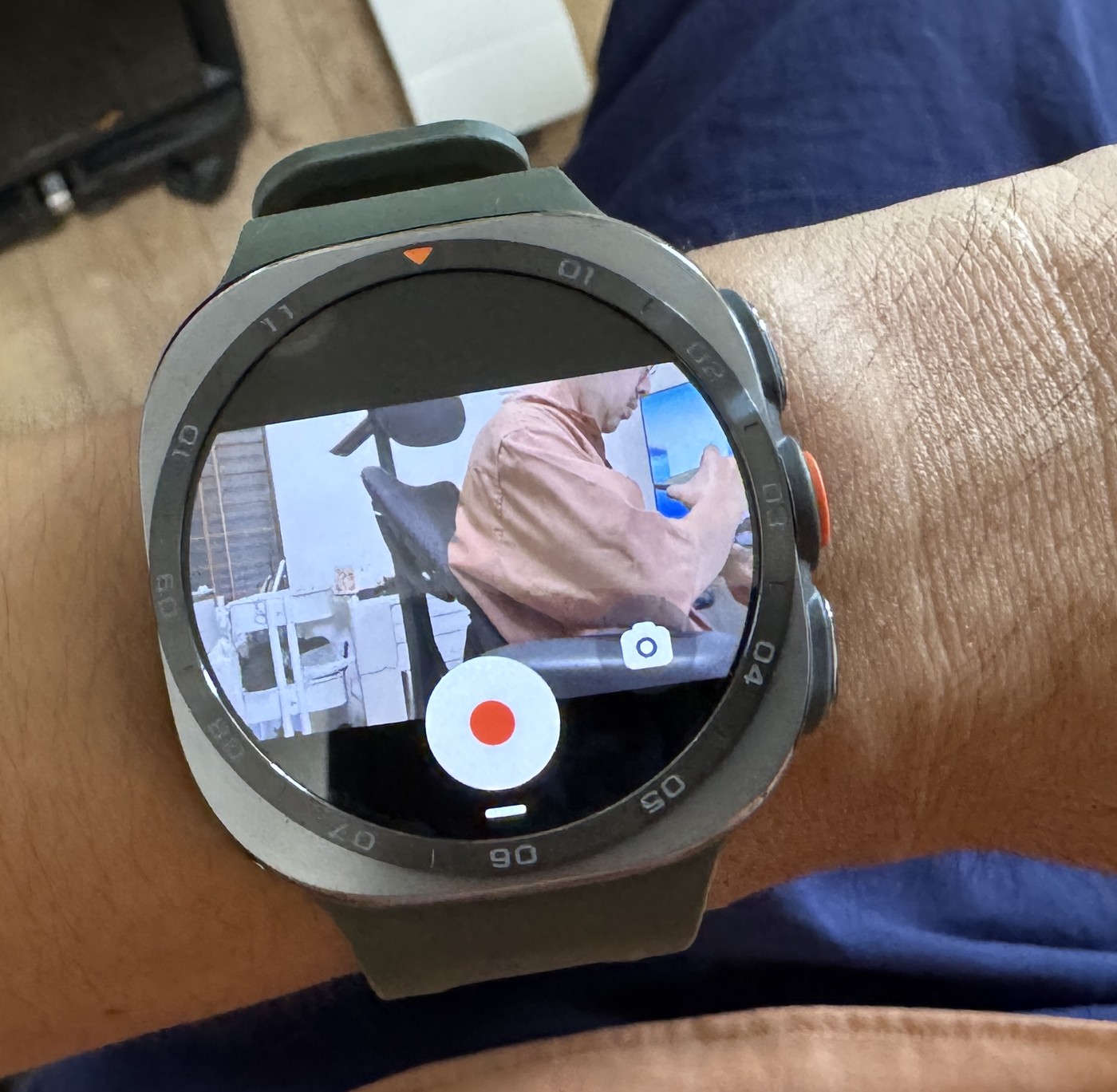 Galaxy Watch Ultra2の画面に、Galaxy Z Flip8のカメラのプレビューが表示されている。下に赤い録画ボタン、その横にカメラ切り替えのアイコンが並ぶ。