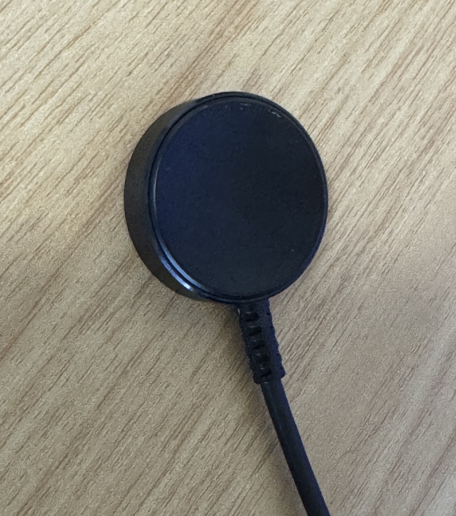 Galaxy Watch Ultra2に付属するワイヤレス充電器。ケーブル一体型の黒い円盤で、木のテーブルに置かれている。
