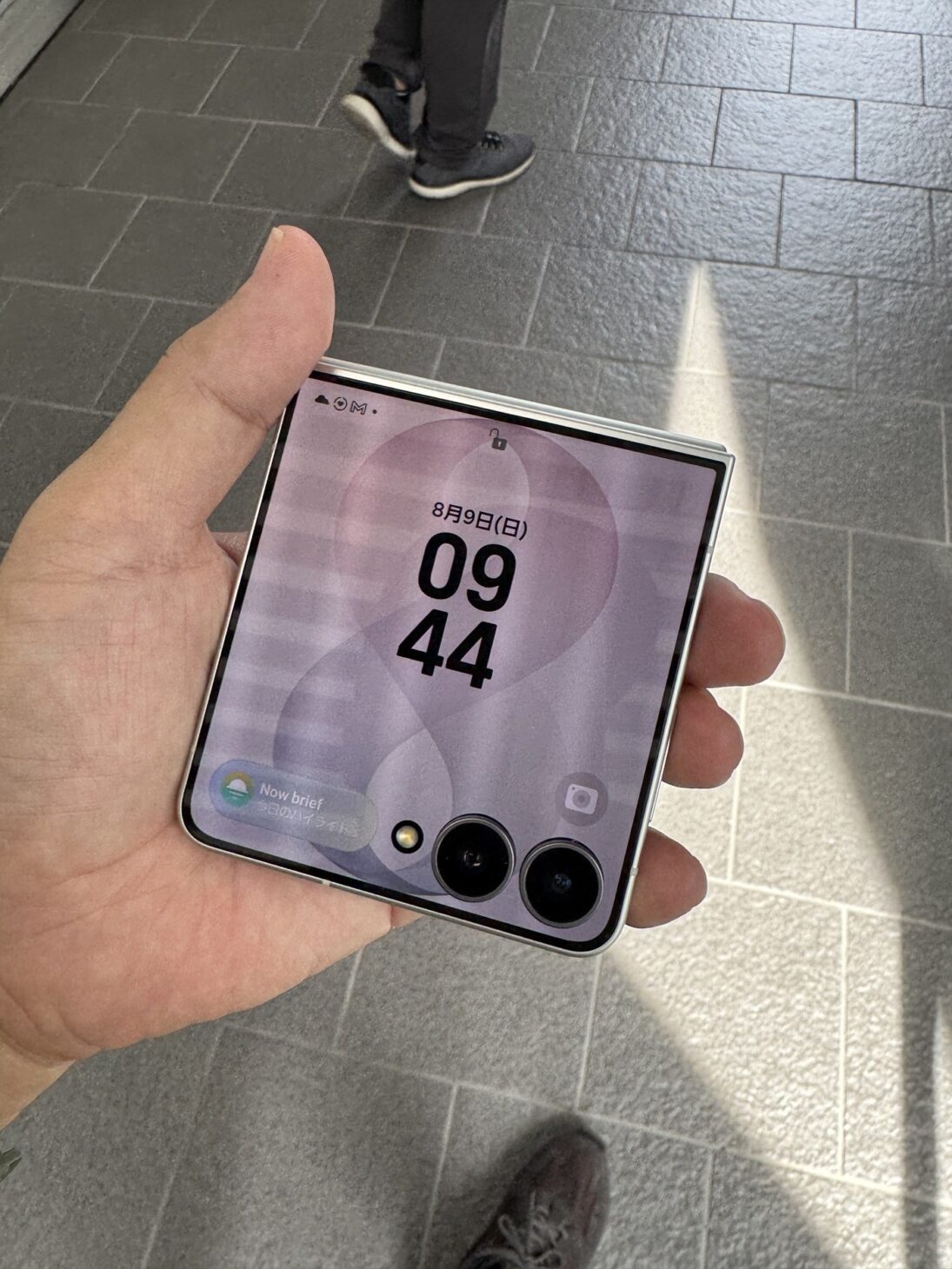 Galaxy Z Flip8を閉じた状態で手のひらに載せたところ。約4.1インチのカバー画面に時刻とNow briefが表示されている。