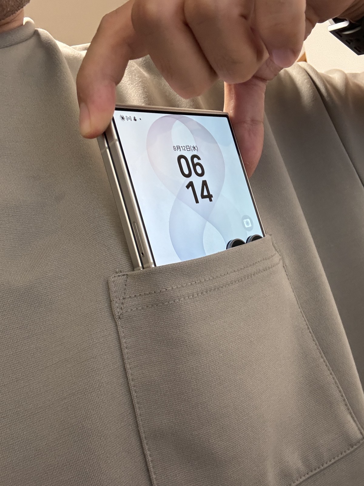 Galaxy Z Flip8を閉じてTシャツの胸ポケットに入れているところ。6.9インチの画面を持つスマートフォンが胸ポケットに収まっている。