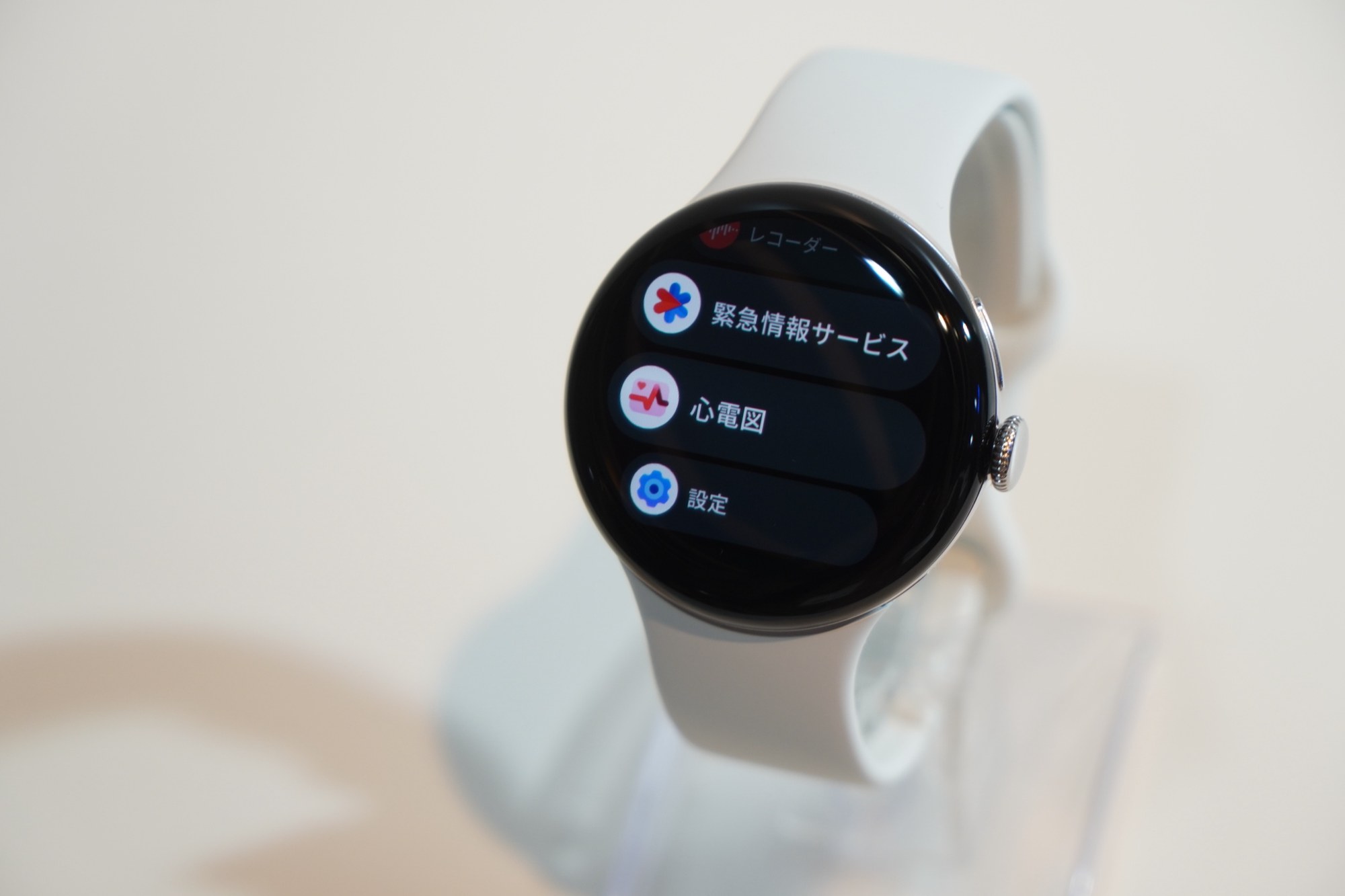白いバンドの Pixel Watch 5 の画面に緊急情報サービス、心電図、レコーダー、設定のアイコンが並んでいる