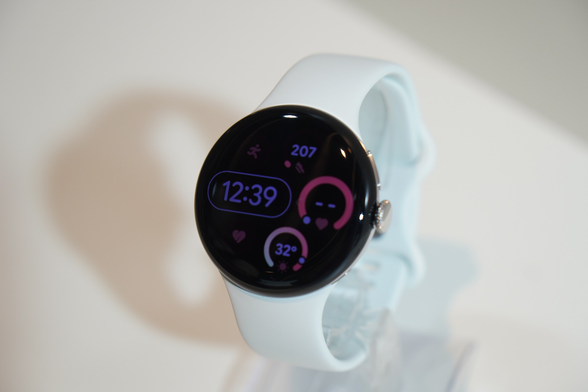 白いバンドの Pixel Watch 5 が 12時39分の文字盤に歩数 207 と気温 32 度を表示している