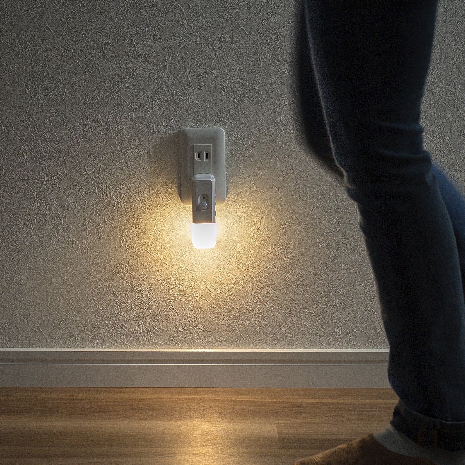 夜の廊下でコンセントに挿したLED-SL2が人の接近を感知して点灯し、足元を電球色で照らしている様子