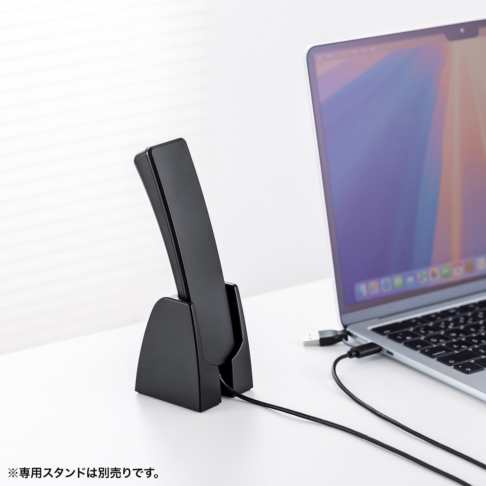 デスクの上でノートパソコンの横に置かれた受話器型ハンドセット用スタンド。