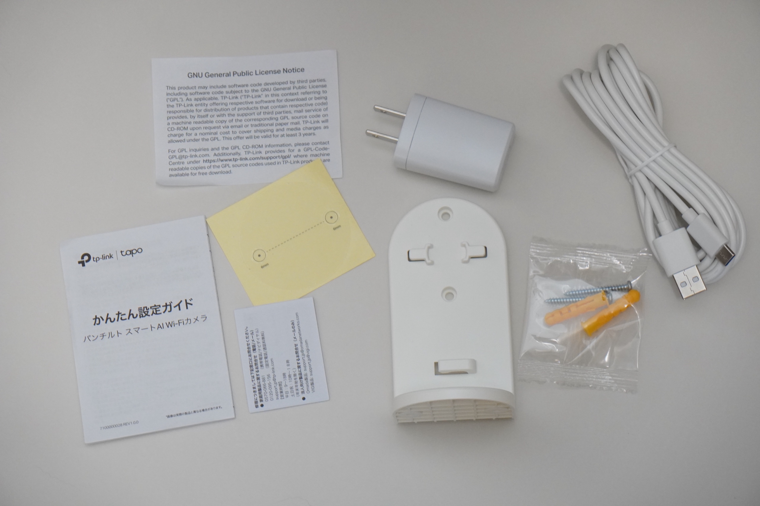 Tapo C260の同梱物一式を白背景で並べた俯瞰。かんたん設定ガイド・位置決めシール・電源アダプター・壁取り付けプレート・ネジとアンカー・長めのUSBケーブル