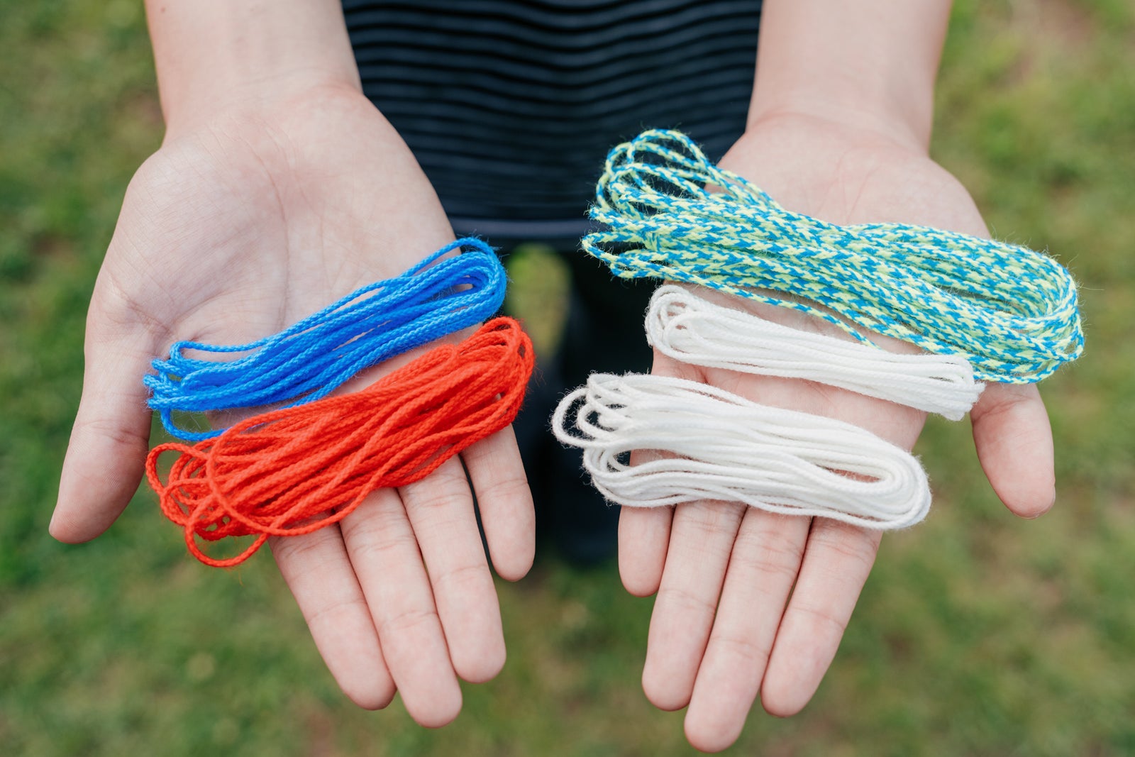 ZipString Aracnaに同梱される、ネオンカラー3本とグローストリング2本の合計5本のヒモを両手に載せたところ