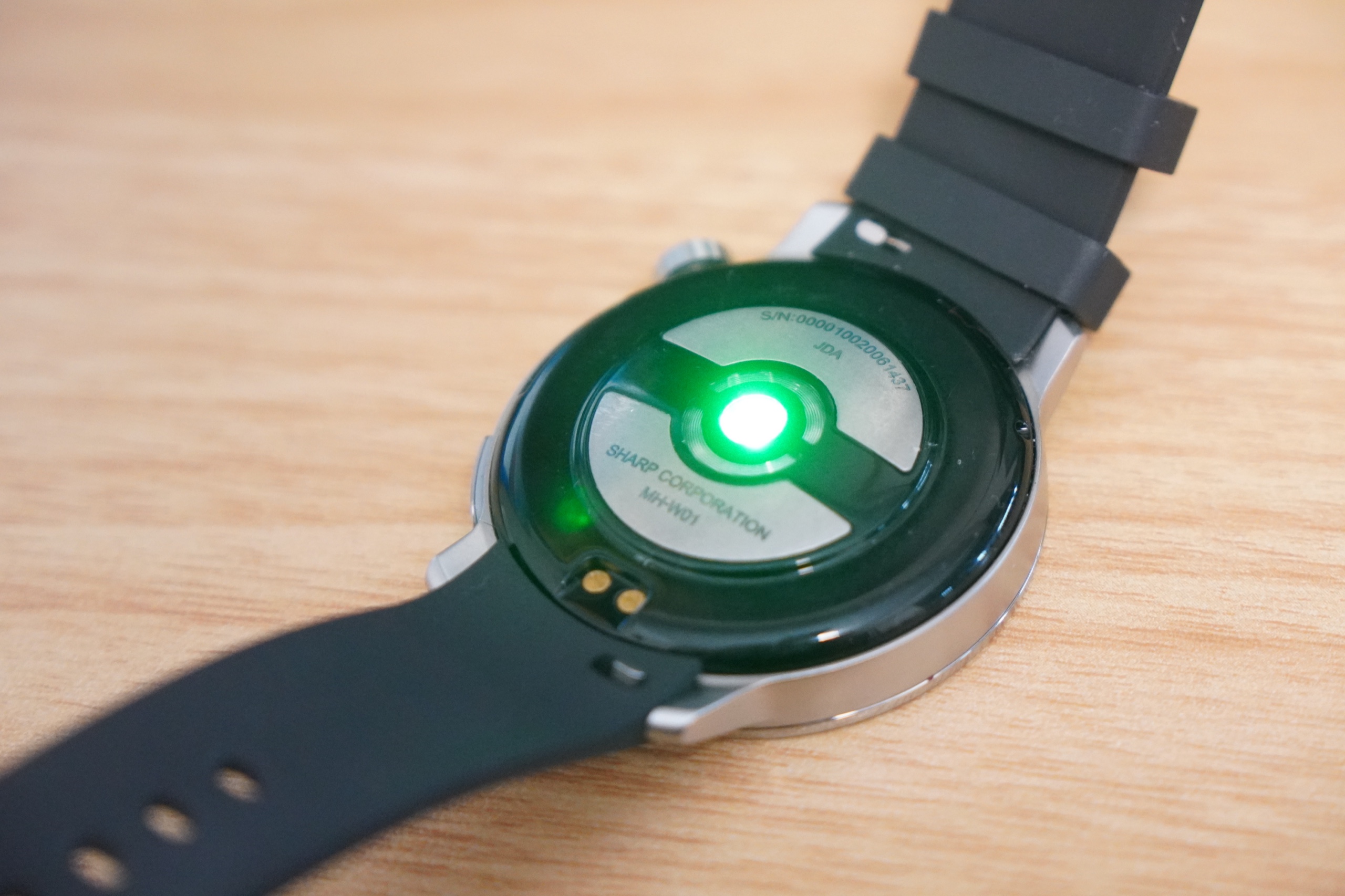 シャープ「からだメイト Watch」の背面。中央の光学式心拍センサーが緑色に発光し、周囲に生体電気インピーダンス測定用の電極と充電端子が並ぶ