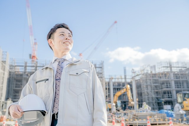 建設現場でヘルメットを手に立つ作業服姿の男性。2025年6月施行の熱中症対策義務化のイメージ