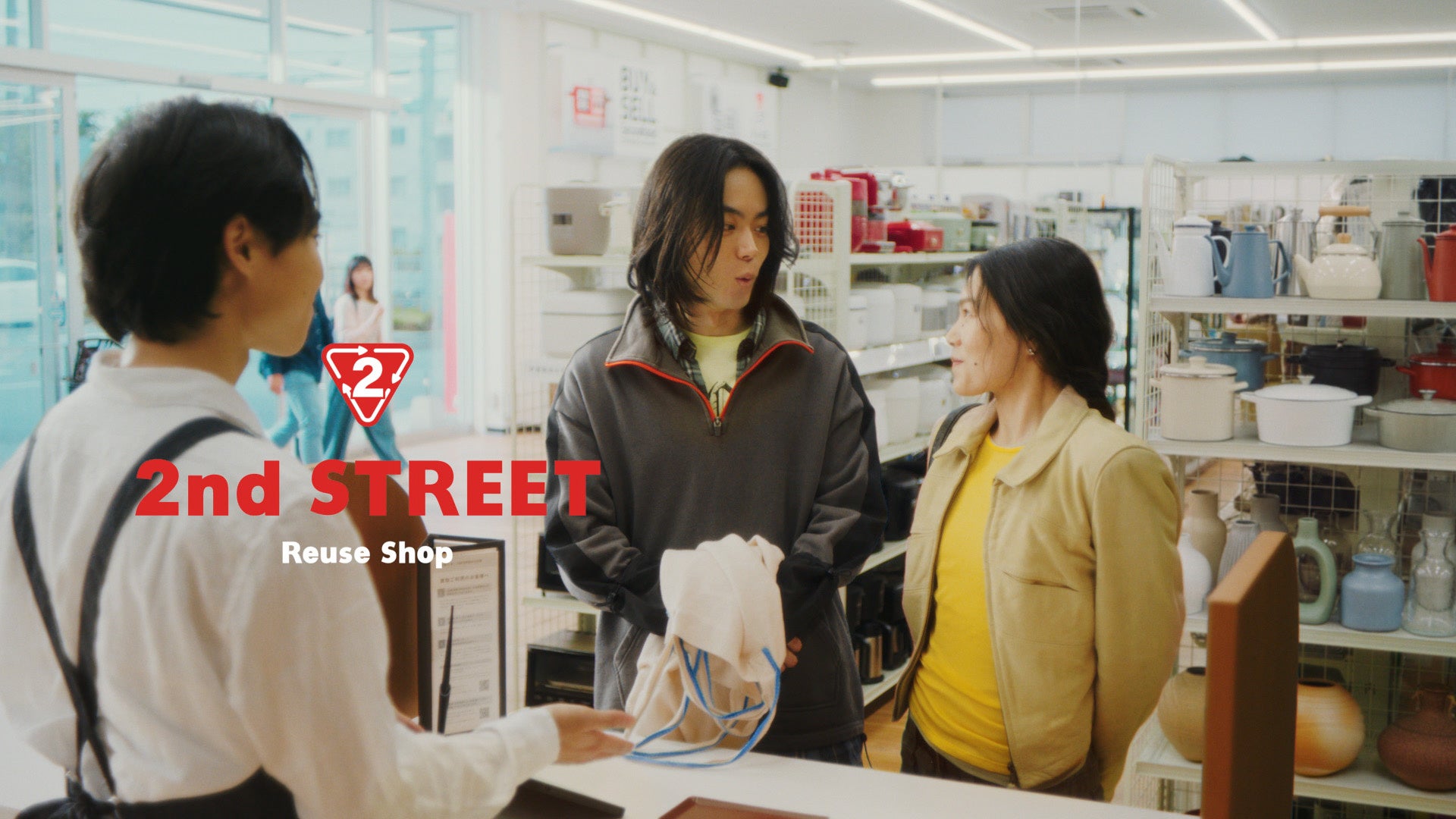 セカンドストリートの買取カウンターで、菅田将暉さんと山本奈衣瑠さんが店員と向き合っている場面