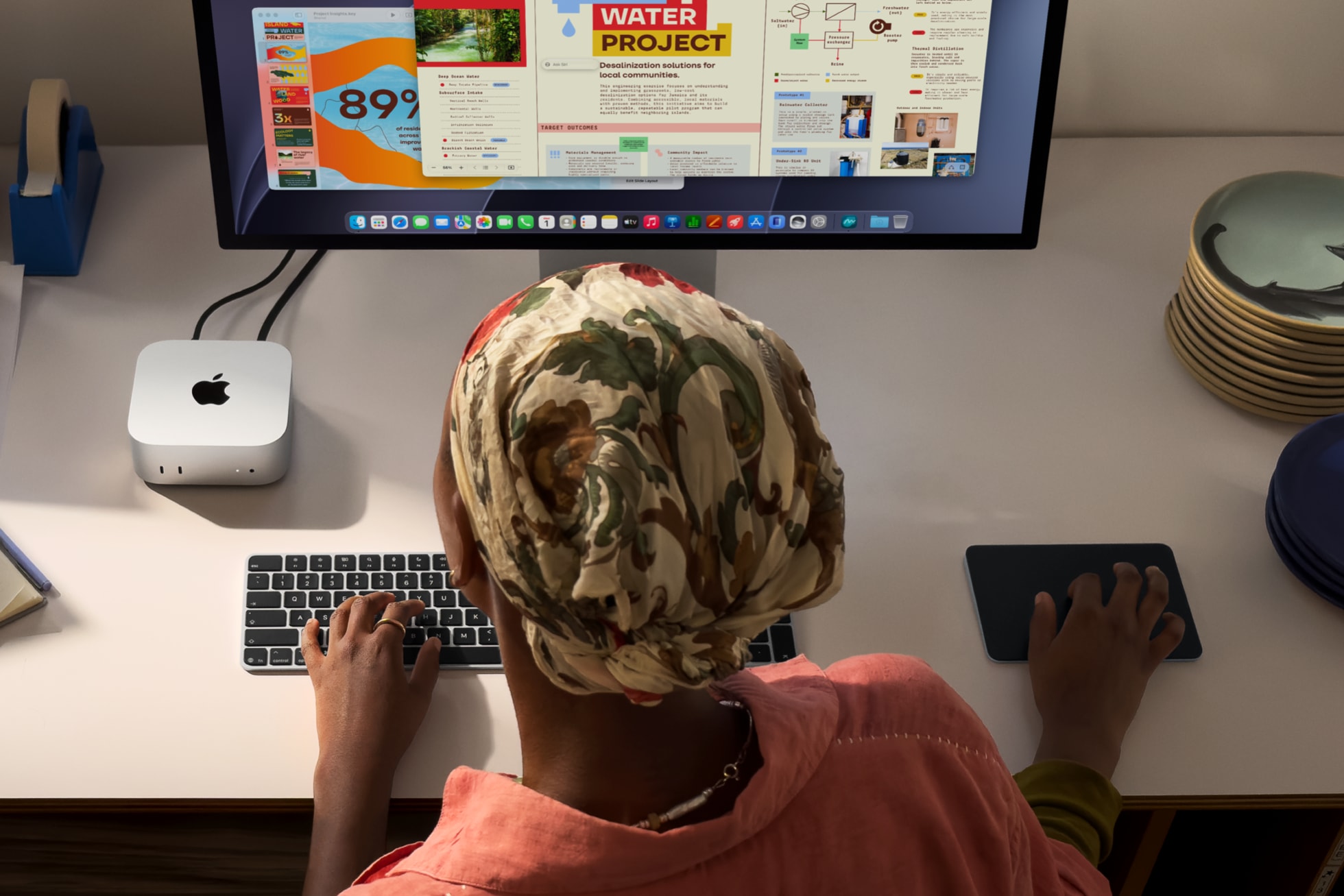 机に置いたMac miniを外部ディスプレイとキーボード、トラックパッドにつないで作業している様子。画面にはプレゼン資料が開かれている