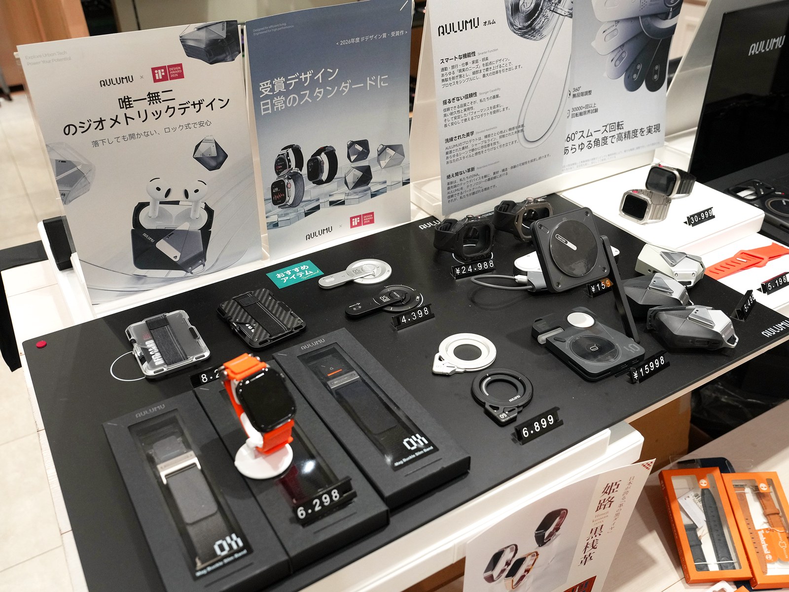 AULUMUのMagSafe対応アクセサリーやApple Watch用ケースを並べた展示台。製品説明のパネルと価格札が置かれている