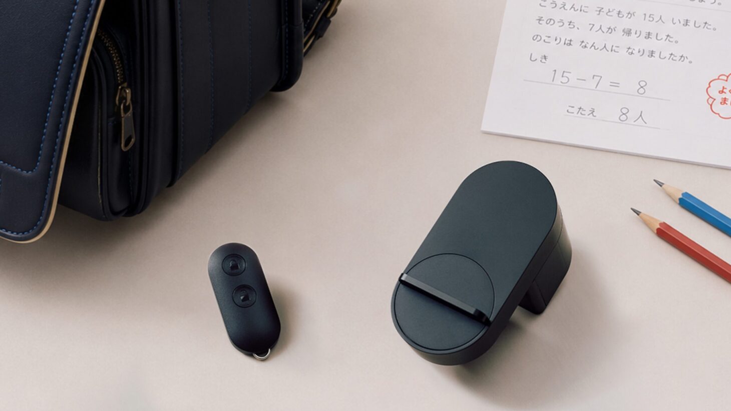 ランドセルと算数のプリントが置かれた机に、スマートキー「Nature Key」とスマートロック「Nature Lock」本体が並ぶ