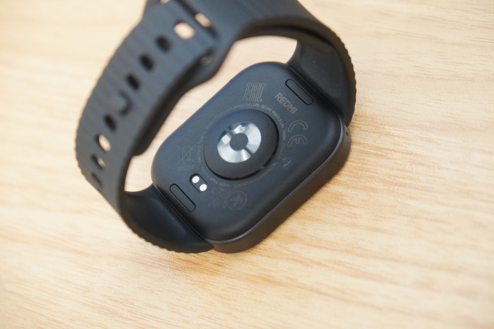 REDMI Watch 6 Liteの裏面。中央に心拍センサー、REDMIの刻印、下部に磁気充電用の2つの接点が見える