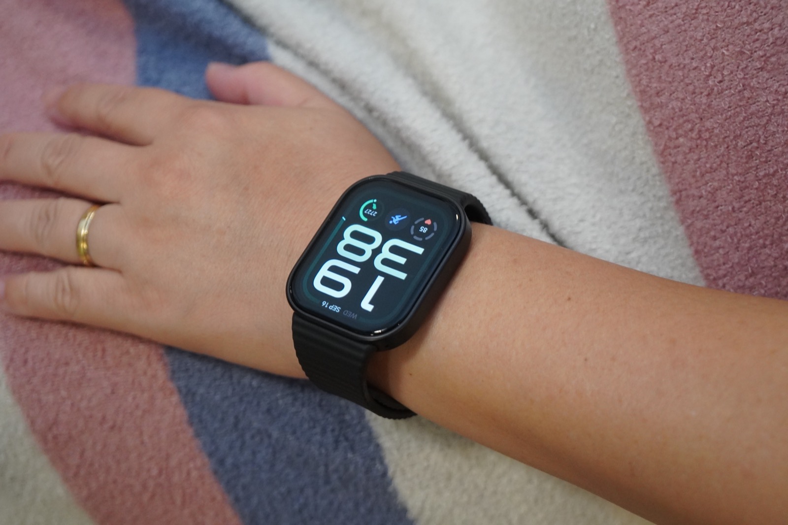 ブランケットの上に置いた腕にREDMI Watch 6 Liteを装着した様子。画面に19:38と表示されている