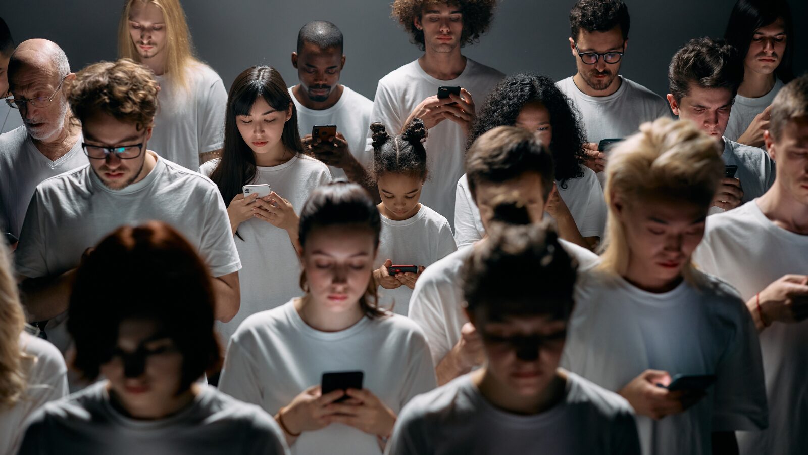 白いシャツを着た大勢の人がうつむいてスマートフォンを見つめているイメージ写真