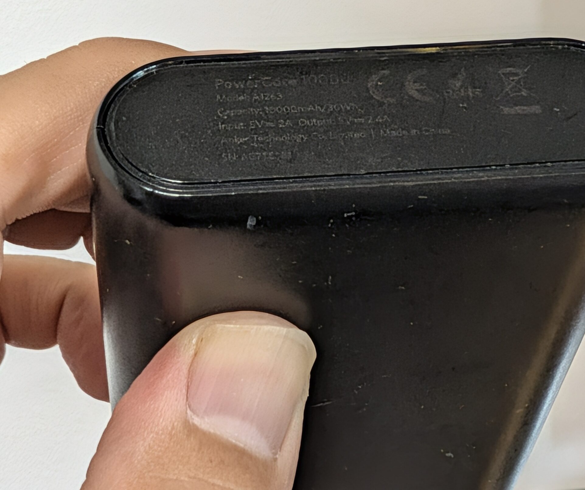 使い込んだAnker PowerCore 10000を手に持ち、斜めに傾けて側面の印字に光を当てたところ。PowerCore 10000、Model A1263、容量、SNの各行が浮かび上がって読める
