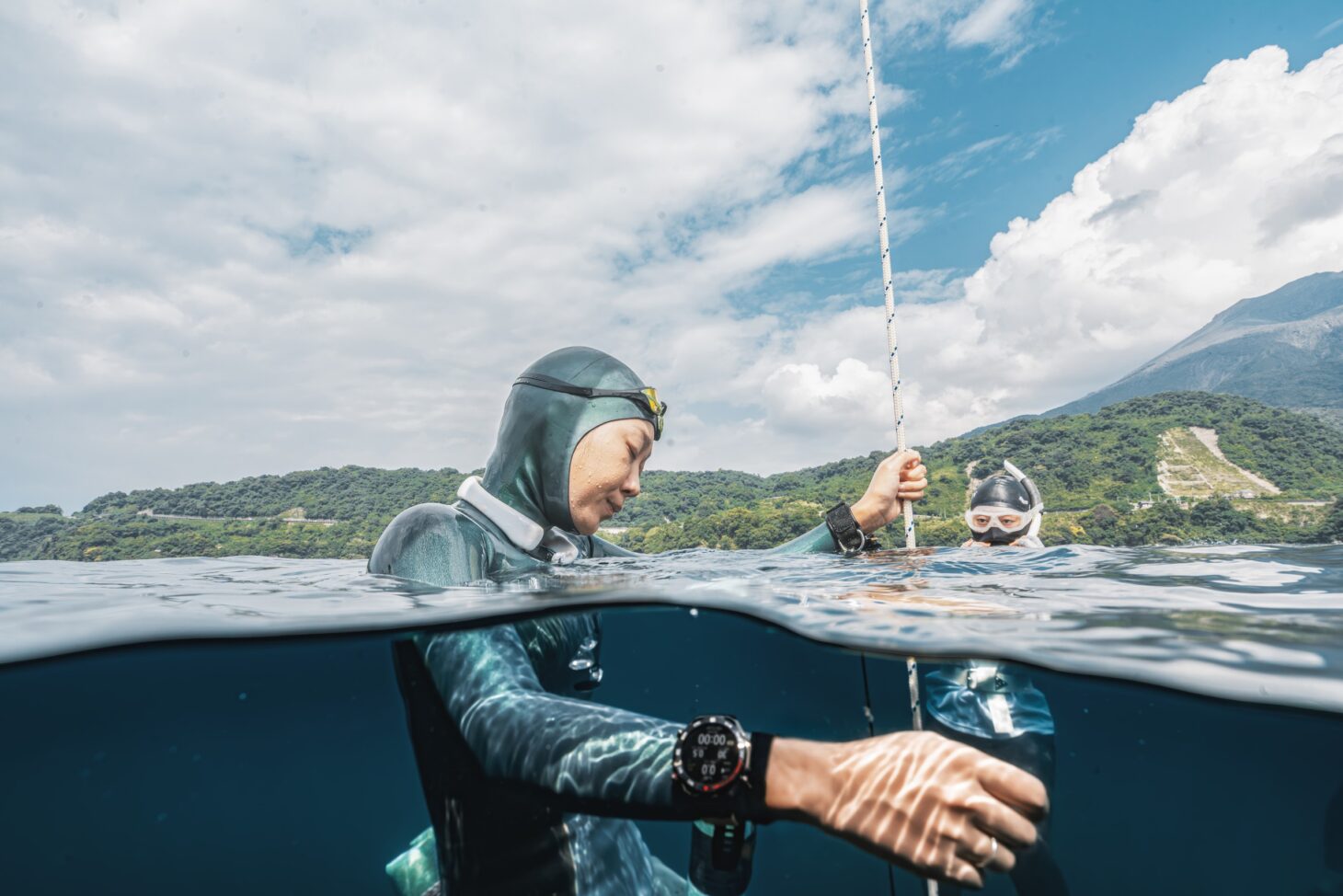 Volcano Cup 2026の会場で、HUAWEI WATCH Ultimate 2を腕に着けて水面でロープにつかまるフリーダイバー。背景に桜島が見える