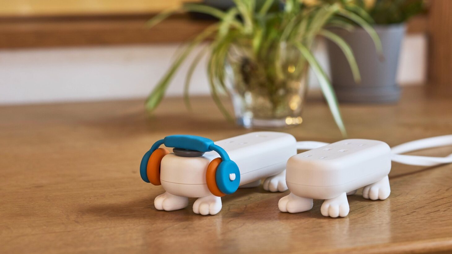 木製デスクに置かれた4本脚の白い電源タップ「モンタップ」2台。左はヘッドホン型のフィギュアキャップ付き