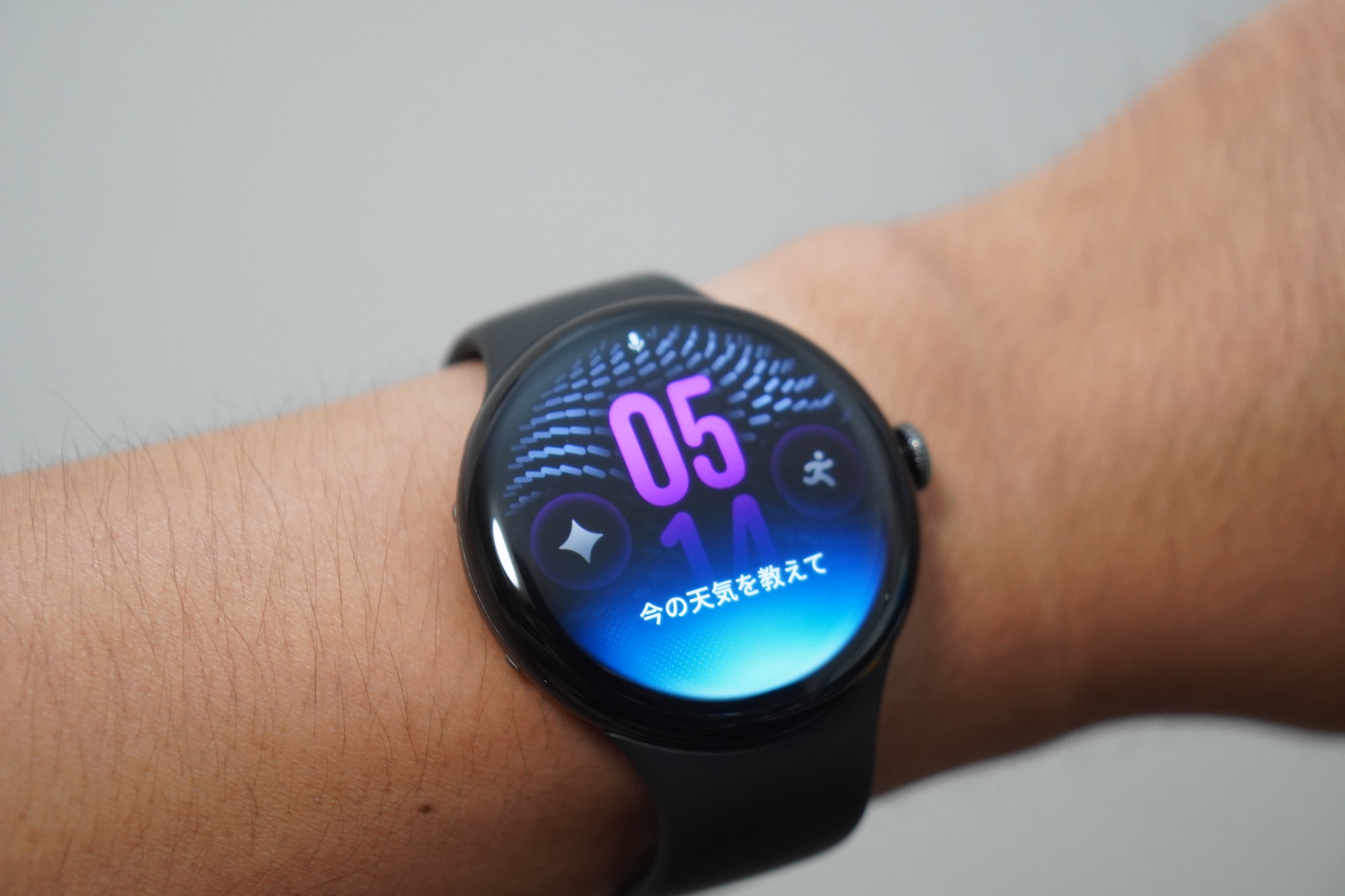 腕に着けたPixel Watch 5にGeminiで話しかけている画面。マイクのアイコンの下に「今の天気を教えて」と認識された文字が出ている