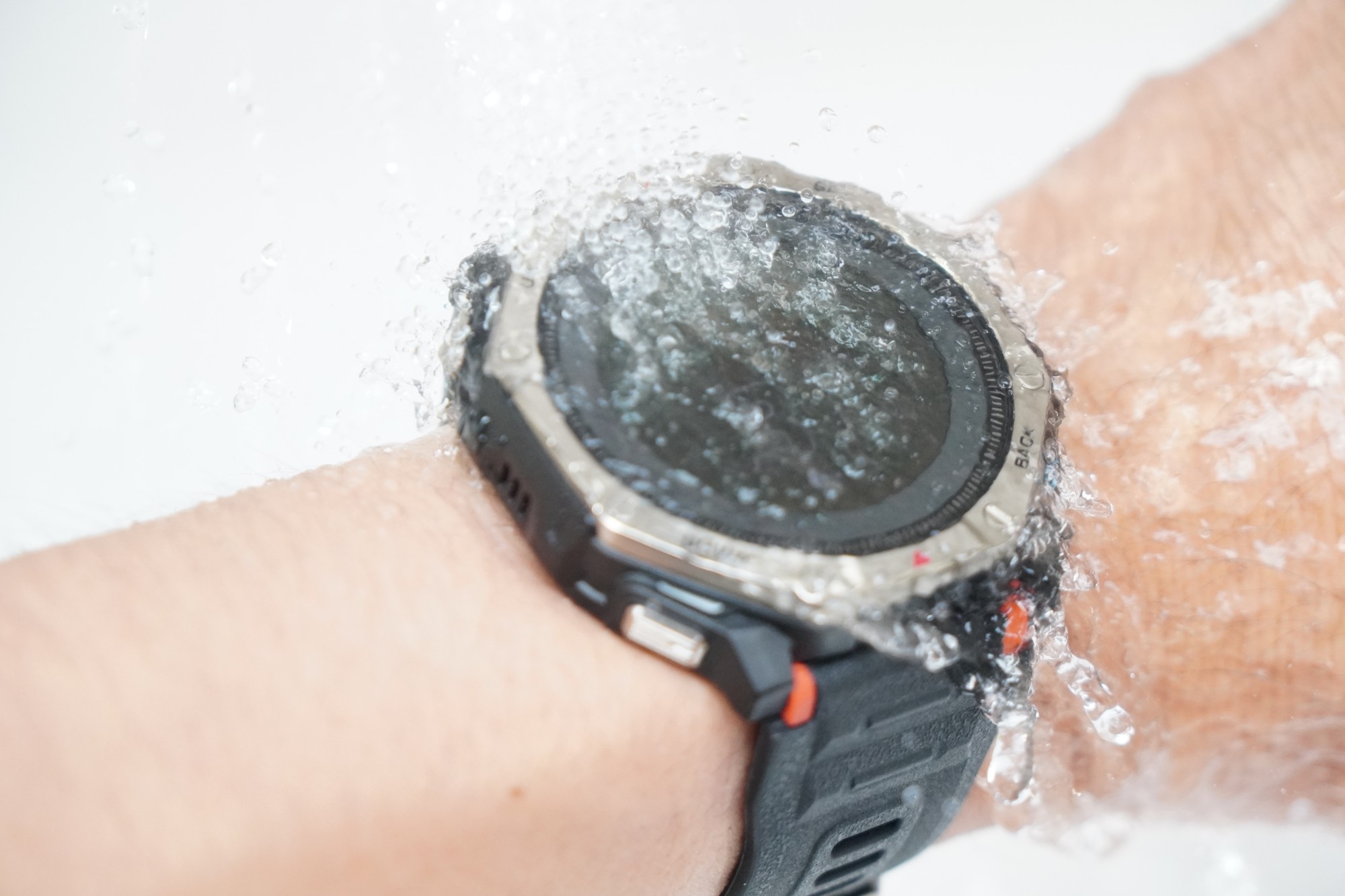 腕に着けたAmazfit T-Rex Dual Solarに水道の水をかけているところ。画面の上を水が流れている
