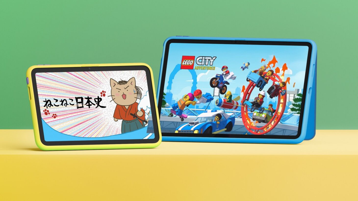 黄色い台の上に並んだ2台のAmazon キッズ タブレット。画面にアプリが表示され、専用カバーのスタンドで立てられている