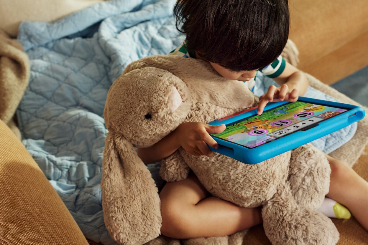 ぬいぐるみを抱えながら青いカバーのAmazon キッズ タブレットを操作する子ども