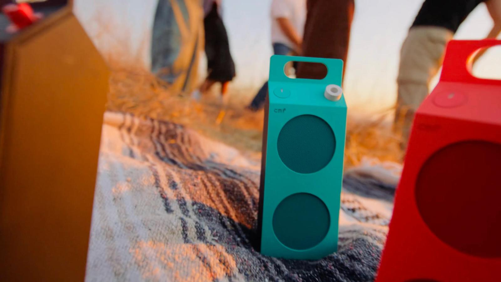 屋外の敷物の上に置かれたターコイズとオレンジのCMF Speaker M