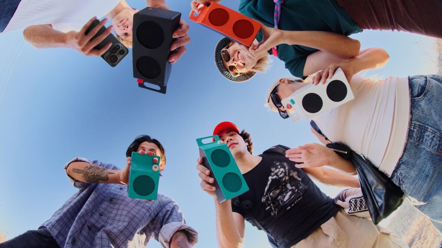 4色のCMF Speaker SとCMF Speaker Mを、輪になった若者たちが空に向けて掲げている写真