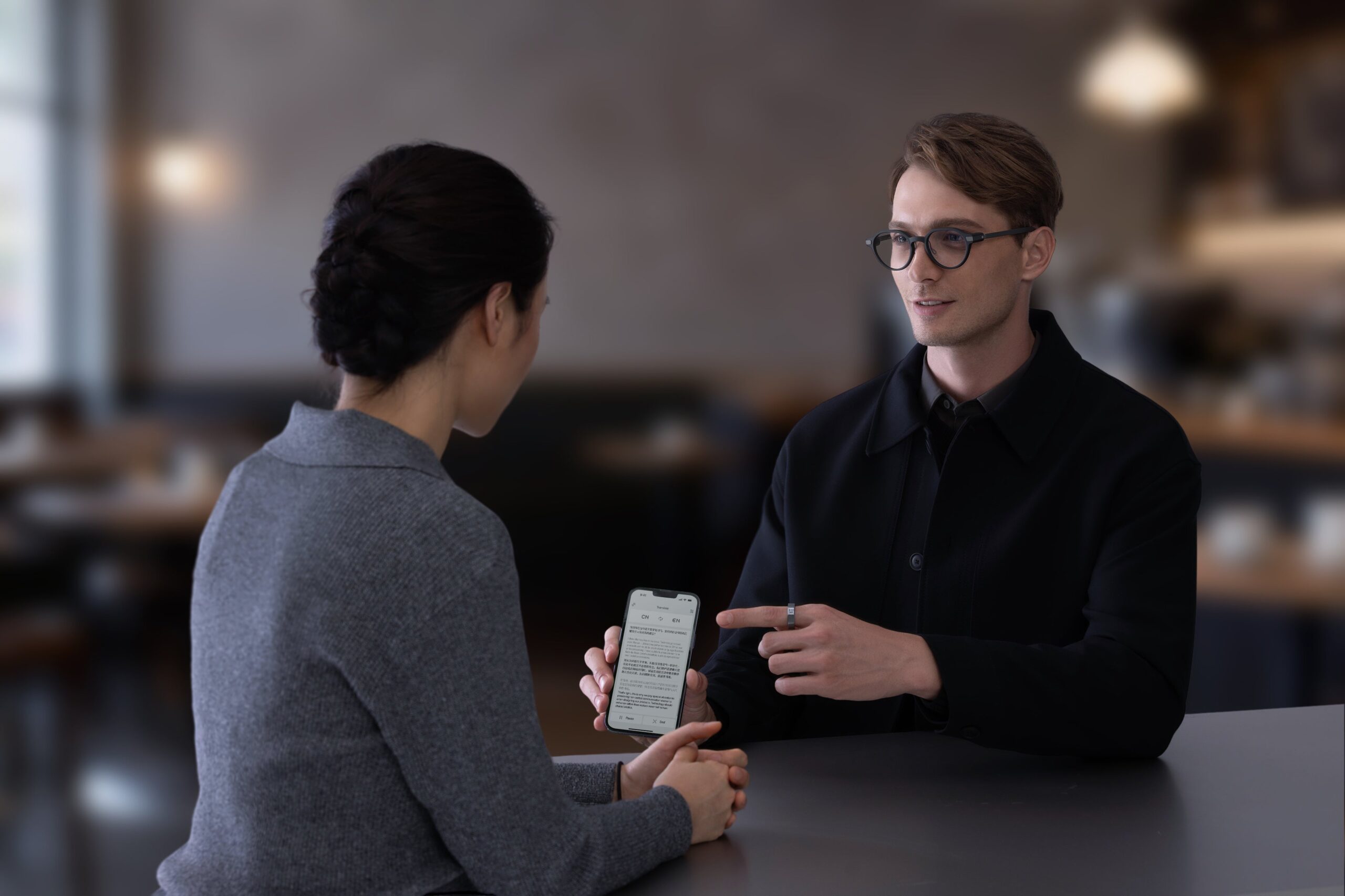 Even G2を掛けた男性が、スマートフォンを手にした女性とテーブルを挟んで話している場面