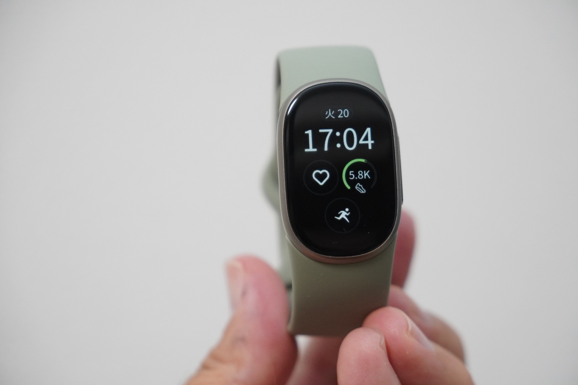 手に持ったGoogle Fitbit Edgeの正面。シャンパン系の金属ケースに縦長の画面があり、日付と17:04の時刻、歩数が表示されている。バンドは淡いグリーン