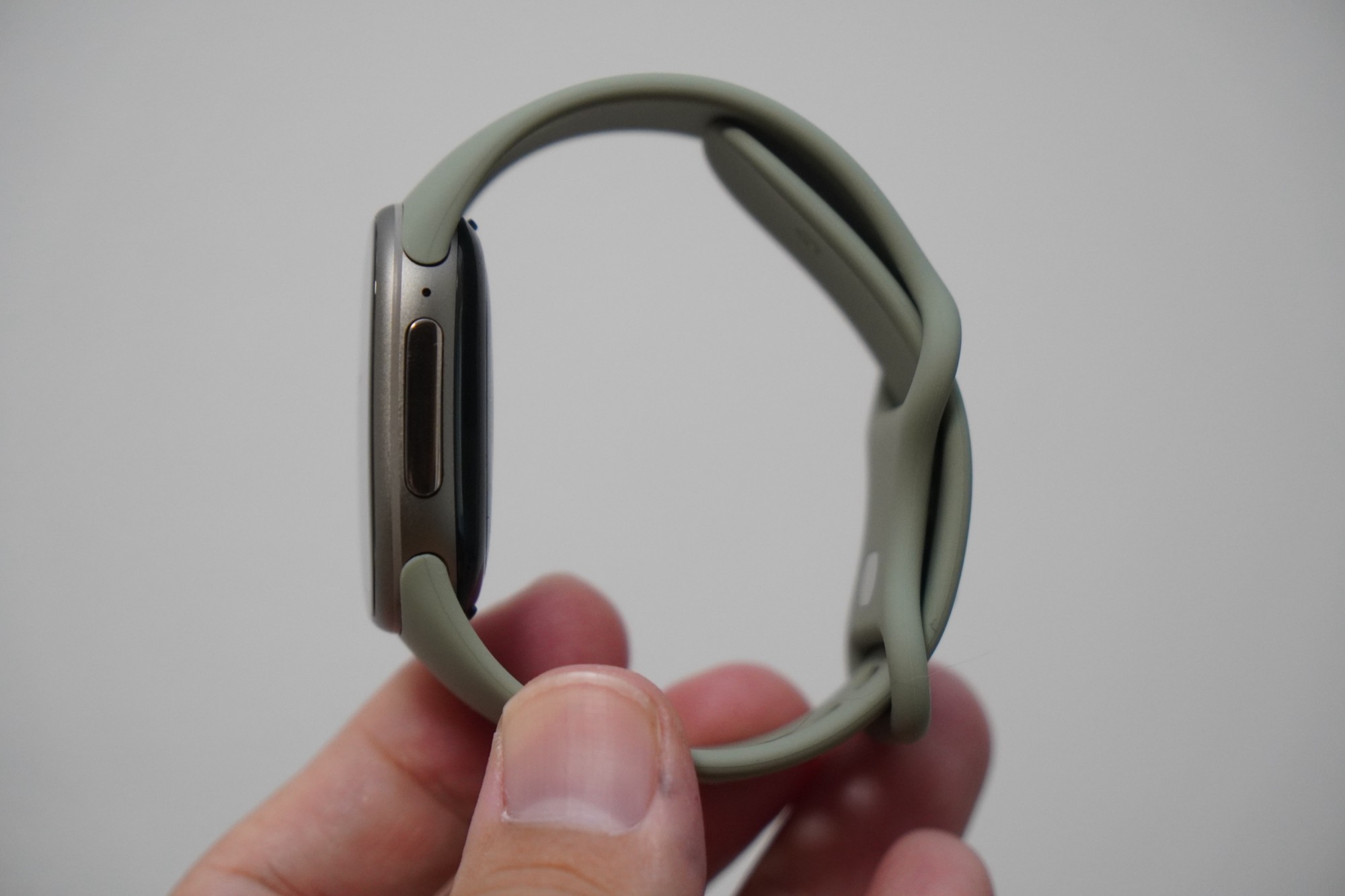 バンドを輪にしたGoogle Fitbit Edgeを手に持ち、真横から見たところ。金属のケースの厚みとサイドボタンが見える