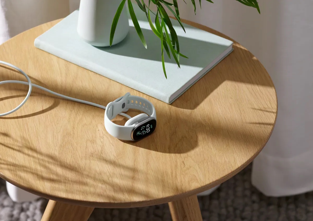 木のサイドテーブルの上で、白いバンドのGoogle Fitbit EdgeをUSB-Cケーブルで充電している様子
