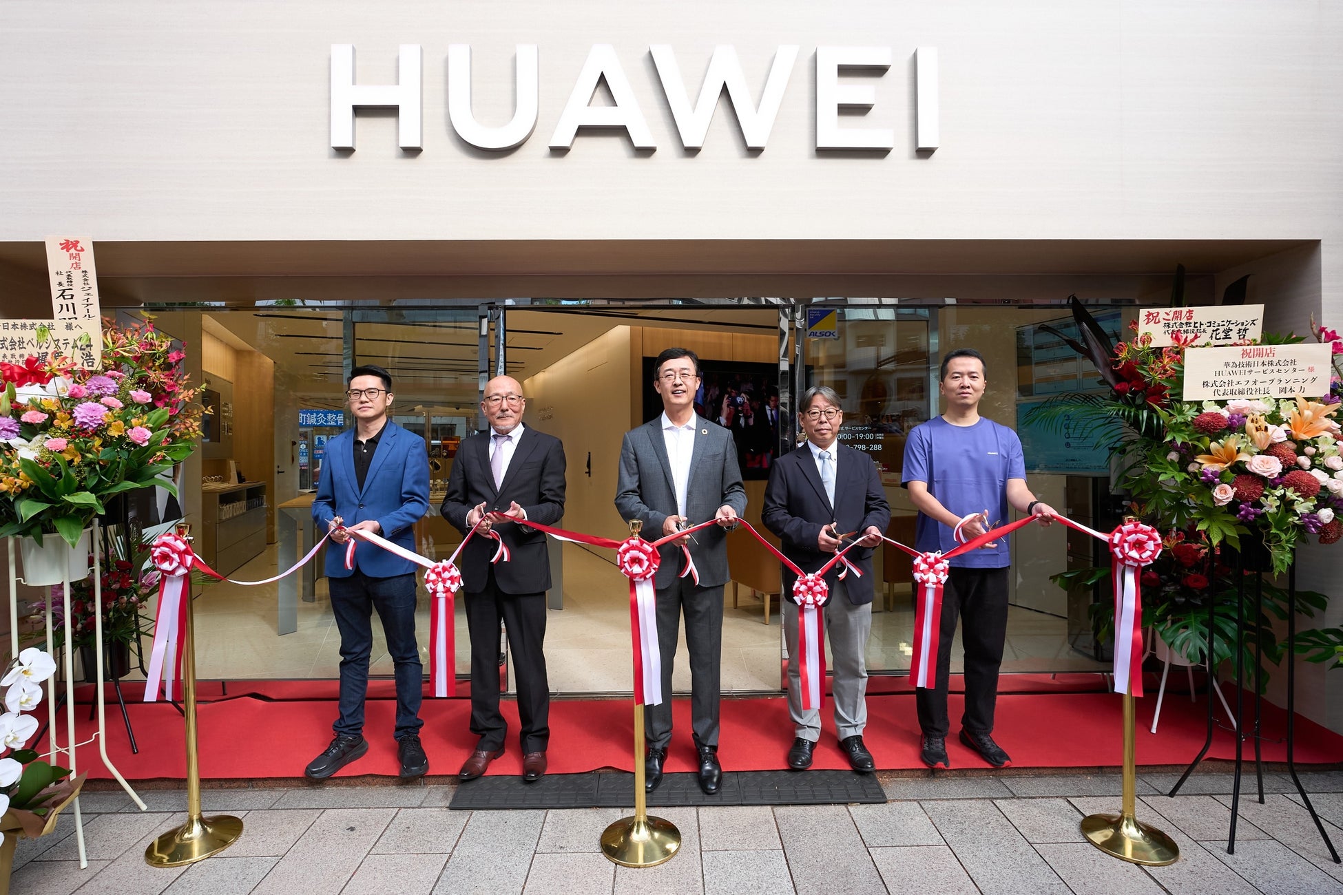 HUAWEI公式サービスセンターの入口前で、ファーウェイと日本マニュファクチャリングサービスの5人がテープカットをするオープニングセレモニー