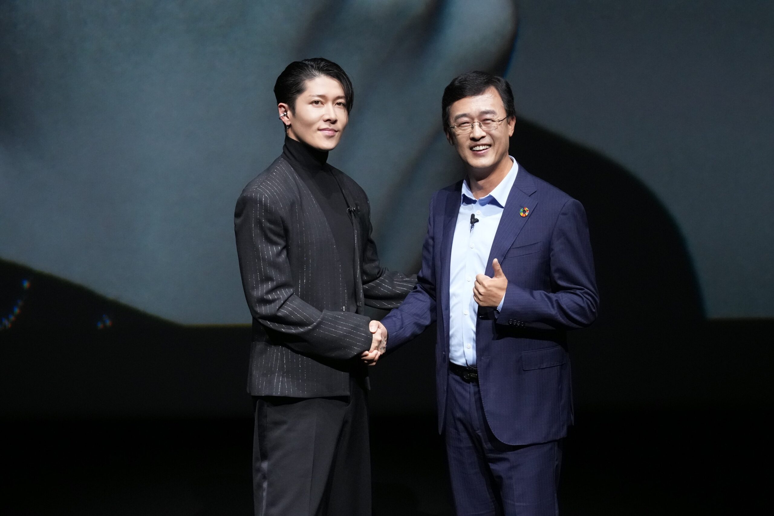 発表会のステージで握手するギタリストのMIYAVI氏とファーウェイデバイス日本・韓国リージョンの賀磊プレジデント